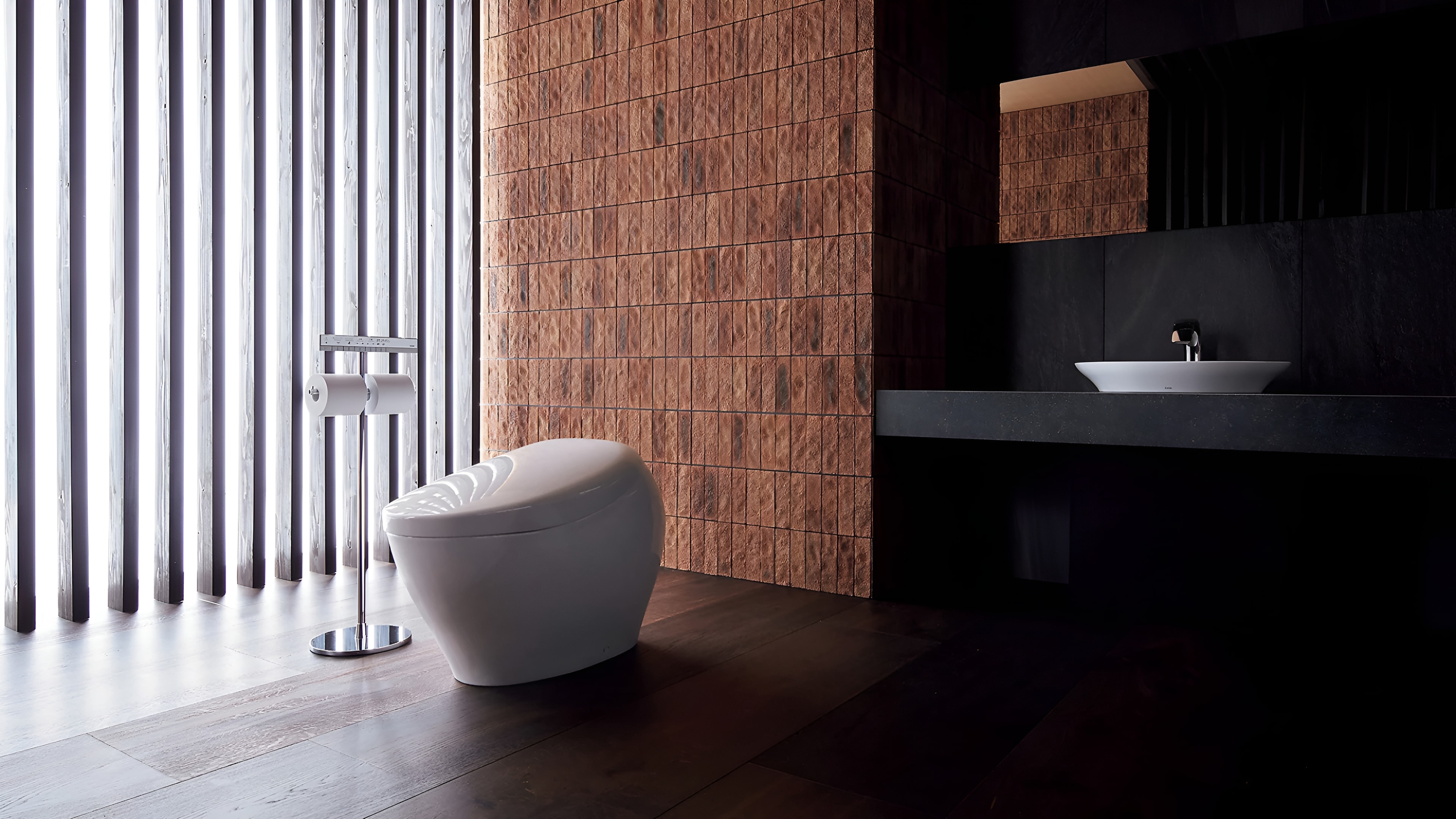 Modern bathroom with a freestanding white toilet, dark vanity, and warm brick tile